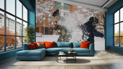 Mother and son throw snowballs at each other during a snowfall. They are both very warm with gloves, scarf, winter hat and COVID mask. Lifestyle Wall mural