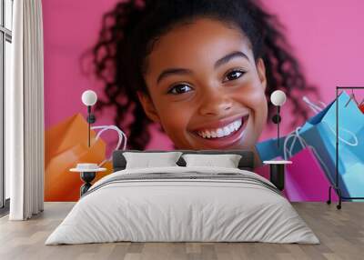 2408 42.A close-up shot of a young woman smiling with excitement, holding multiple colorful shopping bags in front of a pink background. Her cheerful expression and the vibrant colors of the bags Wall mural