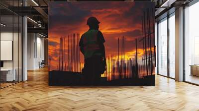 29.Worker in a safety vest at sunset, positioning steel rebar, dark silhouettes of scaffolding, orange glow highlighting edges, high contrast between the vibrant sky and rugged construction materials Wall mural