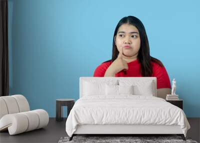 Portrait girl young woman asian chubby fat cute beautiful pretty one person wearing a red shirt is sitting, looking, and thinking idea  suspiciously and seriously  isolated blue background Wall mural