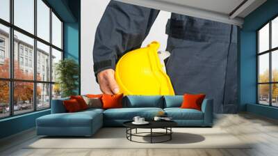 Worker standing in blue coverall holding hardhat Wall mural