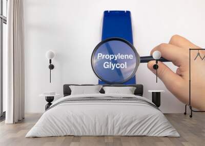 Chemical components on the shampoo label: Propylene Glycol. A hand holds a blue jar and a magnifier, where the harmful ingredients of a detergent are written in close up. Wall mural