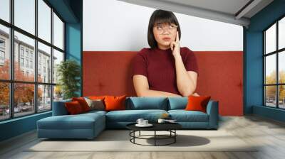 Thinking gesture Young beautiful Asian women dress red shirt and jeans sitting on red couch Wall mural