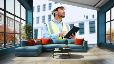 Male engineer checking data on digital tablet and inspecting construction site. Technician in a hardhat doing management and project planning outdoors. Skilled worker looking or overseeing operations Wall mural