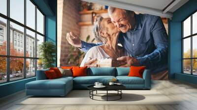 Elderly, couple and happy with gift, surprise and kiss on face together in home. Man, woman and retirement show love, romance and happiness giving present for anniversary, birthday or mothers day Wall mural