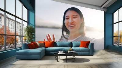 Japanese woman, selfie and happy outdoor, pointing at lake or river for social media and travel influencer in nature. Live streaming, adventure and wave at camera in Japan with smile in portrait Wall mural