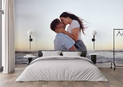 Love, couple and kiss on beach at sunset for romantic and passionate embrace on summer evening date. Dating USA woman and man enjoy dusk sky together at Los Angeles ocean with physical affection. Wall mural