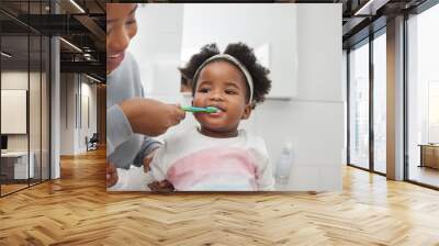 Mom will help her keep her baby teeth clean. Shot of a mother brushing her little daughters teeth in the bathroom at home. Wall mural