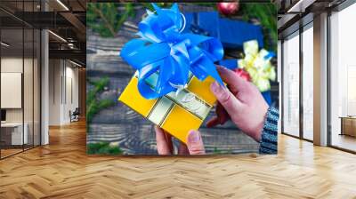 hands holding a gift with a gold ribbon on a wooden background with green branches. place for text Wall mural