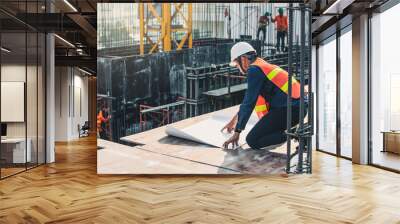 Engineer in hardhat and orange jacket posing on building site. civil engineer or architect with hardhat on construction site checking schedule on plan. Wall mural