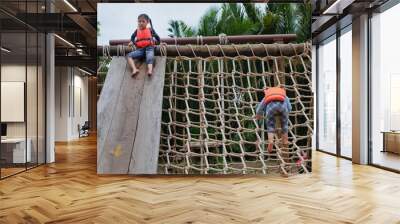 Two cute young Asian girls wearing orange life vest are going up a climbing net in an obstacle course at a summer camp. Wall mural