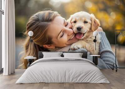 Joyful young adult cradles adorable puppy in her arms, smiling brightly as the little ball of fluff licks her cheek, exuding warmth and happiness. Wall mural