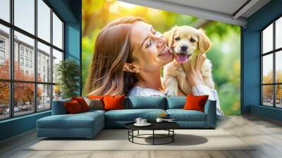 Joyful young adult cradles adorable puppy in her arms, smiling brightly as the playful pup licks her cheek, surrounded by lush green park scenery. Wall mural