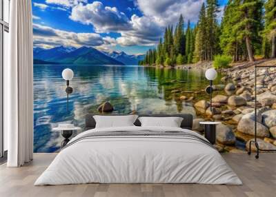 Serenene rocky shoreline of Flathead Lake, Montana, features smooth rounded pebbles and boulders surrounded by lush green forest and majestic mountain peaks in background. Wall mural