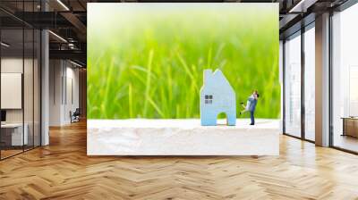 Miniature couple with blue wooden house model over blurred green grass background, real estate business Wall mural