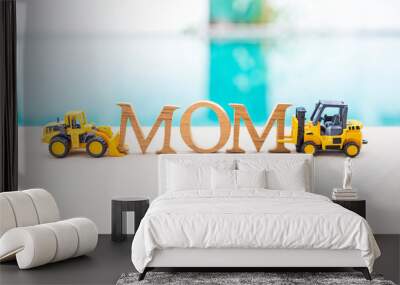 Mom wooden font with two toy truck on swimming pool edge with space on blurred water background, mother's day card background idea, industry style Wall mural