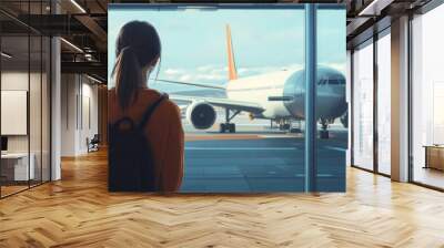 A female traveler standing at the airport window, watching the aircraft as it prepares for takeoff, highlighting the journey ahead Wall mural