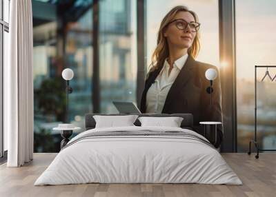 Businesswoman in a suit - Young Caucasian woman wearing a black suit and white shirt. Standing in an office with a background of transparent glass windows showing a view of the city outside. Wall mural