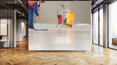 The man in the repairman is holding a mop in a white suit, cleaning the protective clothing of the new epoxy floor in an empty warehouse or car service center. Wall mural