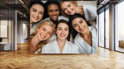 Top view of five women in white bathrobes lying on the bed, smiling looking at the camera, feeling happy. Wall mural