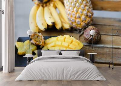 Close up mango with carambola on plate near pine-apple and bananas on wooden table. Wall mural