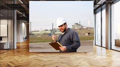 Foreman engineer standing on construction site and holding papers. Wall mural