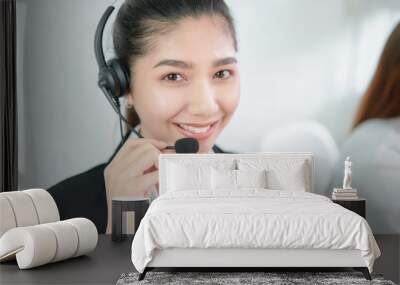 Smiling Asian businesswoman consultant wearing microphone headset of customer support phone operator at workplace. Wall mural