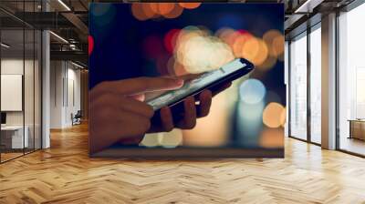 Soft focus of close-up hands using smartphone on bokeh color light in night atmospheric city,  mock up of blank screen. using cell phone on lifestyle. Technology for communication concept. Wall mural