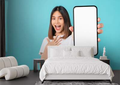 Studio shot of Beautiful Asian woman holding smartphone mockup of blank screen and smiling on blue background. Wall mural