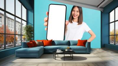 Studio shot of Beautiful Asian woman holding smartphone mockup of blank screen and smiling on blue background. Wall mural