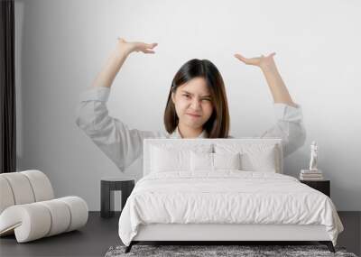 Young Asian woman in white casual clothes attempt to hold something heavy from above. Wall mural