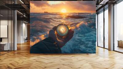 A hand holding a compass in front of a stormy sea at sunset Wall mural