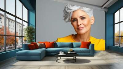 a mature woman with white skin, grey short hair, wavy hair and a clear yellow t shirt, isolated in a light grey studio Wall mural