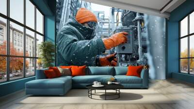 A worker in a winter jacket and gloves operating machinery at a snowy factory site  Wall mural