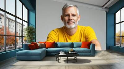 Close up of mature man with white skin, grey short hair, wavy hair and a clear yellow t shirt, isolated in a light grey studio. Portrait person. Wall mural