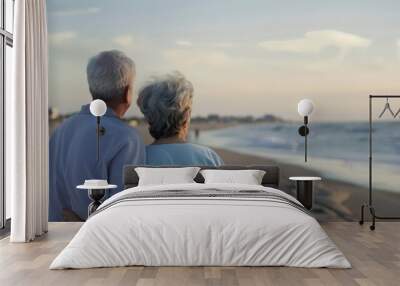 The elderly couple is walking on the beach and watching the sunset. Wall mural