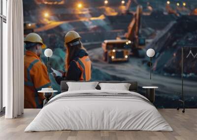 Two mining engineers in hard hats and safety vests discuss plans in front of a large open-pit mine. Wall mural