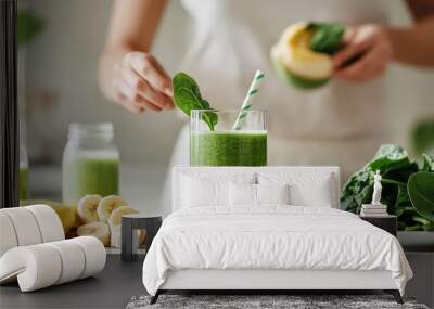 Woman preparing a green smoothie in a bright kitchen, with fresh spinach, bananas, and almond milk Wall mural