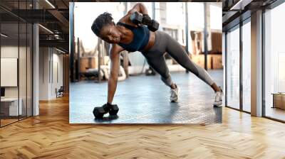 Fitness, dumbbells and woman doing a plank workout in the gym for strength, arm and body training. Sports, challenge and African female athlete doing a muscle exercise with weights in a sport center. Wall mural