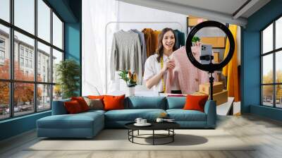 Beautiful woman describe selling clothes on camera live broadcast on social network at home, Online selling clothes on social media. Vlogger woman influencer, SME retail store owner. Wall mural