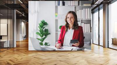 Happy Business woman entrepreneur holding calculator working sit at office desk. Portrait of beautiful smiling young businesswoman working at modern work station. Wall mural