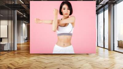 Young sporty woman doing shoulder and arm stretching isolated on pink background. Wall mural