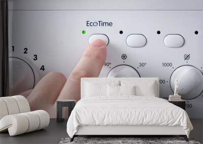 A man's hand pressing the button for selecting the economical washing mode on the panel of the washing machine. Wall mural