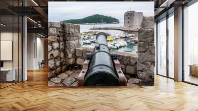 Large cannon jutting out from a fortified castellation, pointing over a coastal town. Wall mural