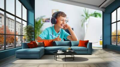 cheerful boy with headphones uses laptop to make a video call with his teacher. Wall mural