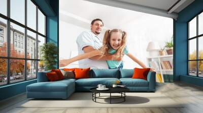 Happy positive cheerful dad is playing with his little charming daughter at home. The man circles and throws the girl up. A dynamic image. Copy space Wall mural