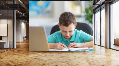 inquisitive boy uses laptop to study school subjects during his online lesson at home. Writing down topic lesson in notebook. E-Education Distance Home Education. Wall mural