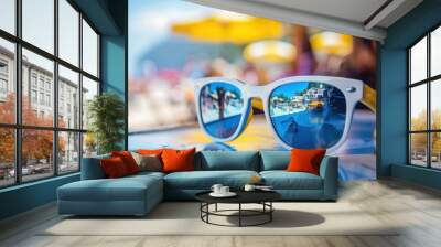 A close-up of the blue, white and yellow sunglasses resting on an outdoor table at a beachside cafe The reflection in one lens shows blurry images of people enjoying summer activities Generative AI Wall mural