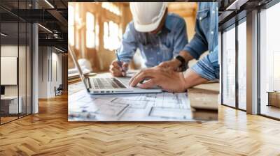 A closeup of two people, one wearing a blue shirt and the other in a white helmet with a laptop on a table looking at construction plans while holding a pencil and paper Generative AI Wall mural