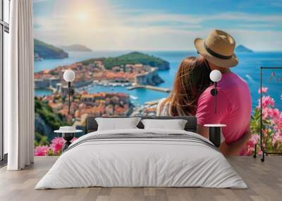 a couple wearing pink shirt and hat, hugging each other while looking at the city of dubrovnik in bl Wall mural